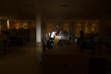 Side view of a tired young woman working at computer in dark office