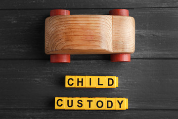Text CHILD CUSTODY made of yellow blocks with toy car on dark wooden background, closeup