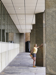 Full length side view of a young woman stretching against pillar in portico