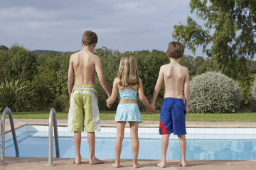 Full length rear view of two brothers and a sister at the edge of a pool