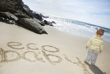 Rear view of baby boy standing by "eco baby" written on sand at beach