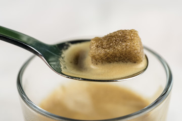 Melting brown sugar cube in a teaspoon of coffee