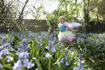 Little young blurred girl in fairy costume running in flower garden