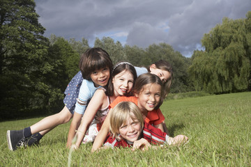 Portrait of five children lying on top of each other in meadow