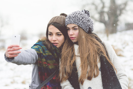 Two female friends taking a selfie outdoors on snowy winter day