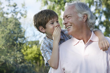 Closeup of a young boy whispering in grandfather's ear outdoors