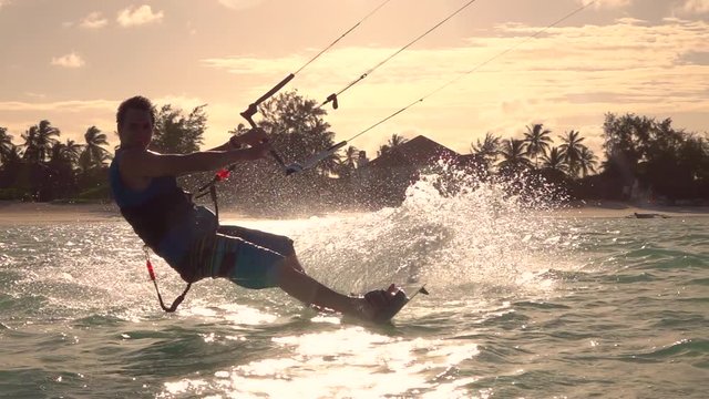 SLOW MOTION: Happy smiling surfer man kiteboarding in tropical lagoon at sunset