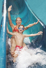 Portrait of a young woman and boy with arms outstretched on water slide