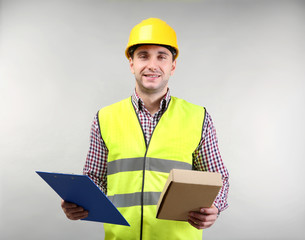 Handsome warehouse worker with clipboard and carton box on light background