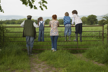 Full length rear view of couple with three children looking at lush landscape by fence
