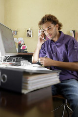 Young African American man using cellphone by computer in the office