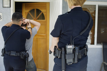 Rear view of police officers arresting young man outside house