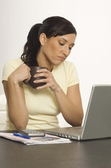 Unhappy Hispanic woman holding coffee cup while looking at laptop