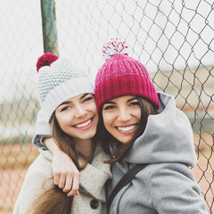 Two teenage girlfriends hugging and smiling outdoors in winter