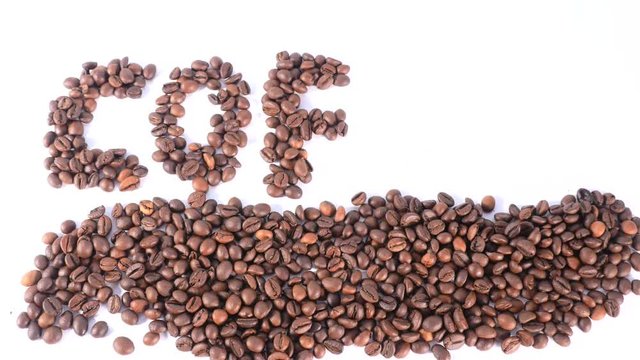 Brown coffee beans lay on white surface and then one by one appear letters making up word coffe, arabica, roasted grain coffee. Close up, stop motion, 4K Ultra HD.