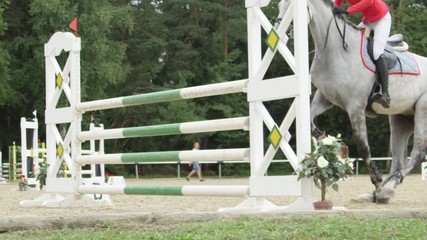 SLOW MOTION: Unrecognizable athlete jumper jumping obstacles with grey horse