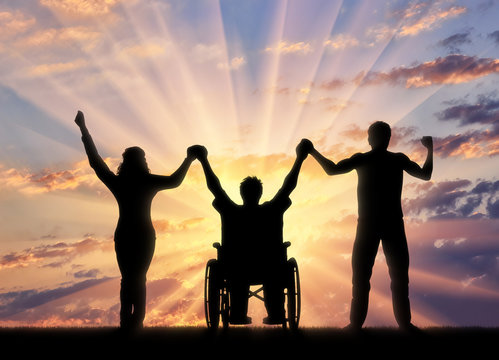 Disabled person in wheelchair and healthy people holding hands on sunset background