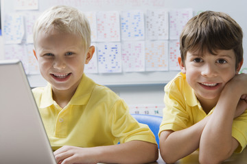 Portrait of happy schoolboys using laptop in classroom
