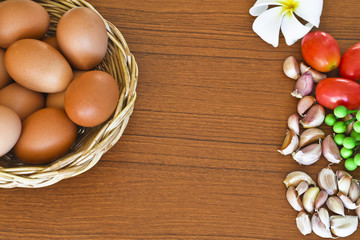 Raw organic brown eggs in wicker basket with ingredients on wood table