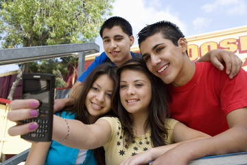 Obraz premium Happy high school friends sitting on steps taking self portrait with cell phone