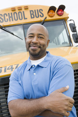 Portrait of a confident teacher with arms crossed standing in front of school bus © MDBPIXS