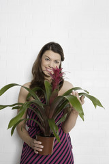 Portrait of young woman holding potted plant against wall