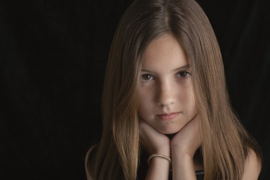 Portrait of young brunette girl resting chin on hands against black background