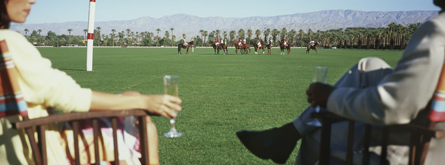 Midsection of couple holding champagne flutes while watching polo match