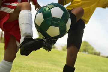 Midsection of two multiethnic player kicking soccer ball
