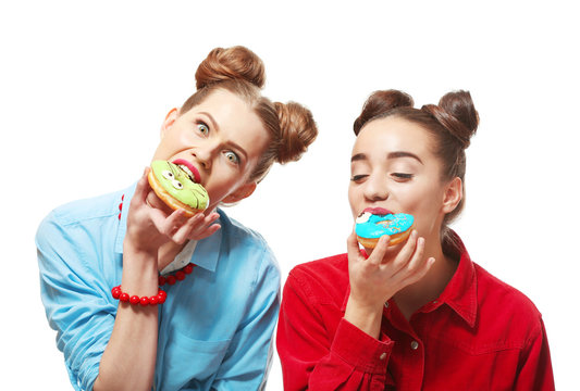 Funny young women eating tasty donuts on white background