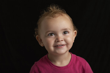 Closeup of smiling baby boy looking away against black background