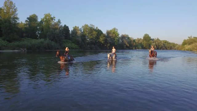 CLOSE UP: Three girlfriends riding horses and standing in the river on sunny day