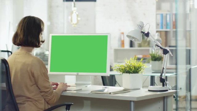 Creative Young Girl Works on Her Desktop Computer. Her Office/ Creative Studio is Brightly Lit. Computer Screen is Green Mock-up. Shot on RED Cinema Camera in 4K (UHD).