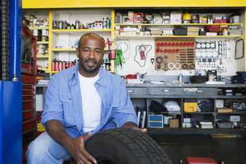 Portrait of a happy African American male mechanic working on a tire