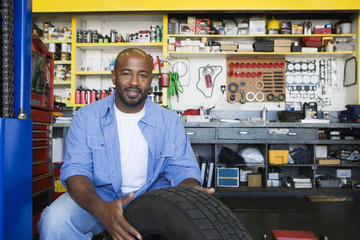 Portrait of a happy African American male mechanic working on a tire - Powered by Adobe