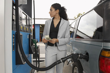 Businesswoman counting money while looking on the meter of petrol pump