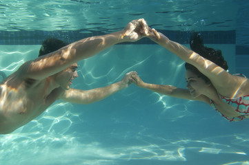 Side view of happy couple holding hands in swimming pool underwater
