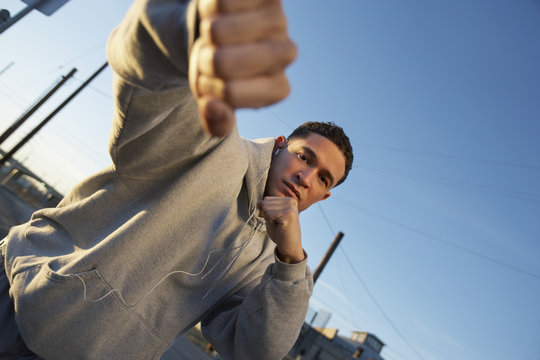 Portrait of male boxer in sweatshirt punching against sky