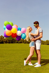 Young happy lovers having date in the park and holding balloons