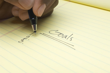 Closeup of man's hand writing list of goals on notepad