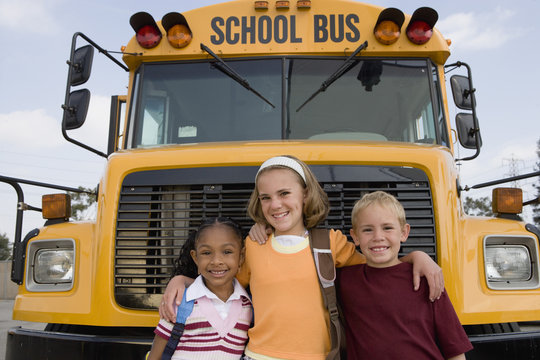 Portrait of happy elementary students standing together in front of school bus