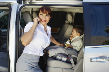 Happy business woman using cell phone with son sitting in car