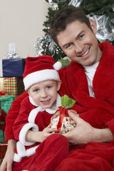 Portrait of happy Caucasian father and son in Santa Claus outfit holding Christmas gift