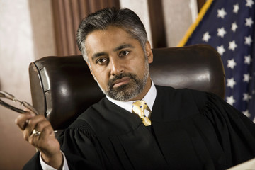 Male judge holding glasses in courtroom