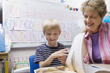 Teacher and cute little boy looking at book in classroom