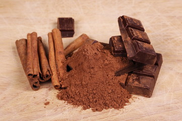 chocolate bars with cinnamon sticks and pile cocoa powder on wooden chopping board