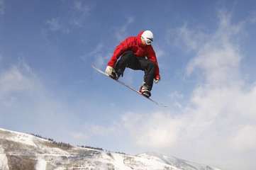 Naklejka na ściany i meble Low angle view of young male snowboarder jumping against cloudy sky