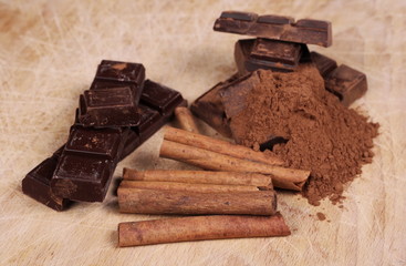 chocolate bars with cinnamon sticks and pile cocoa powder on wooden chopping board