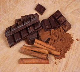 chocolate bars with cinnamon sticks and pile cocoa powder on wooden chopping board