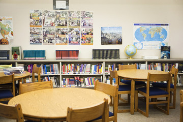 Interior of high school library with arrangement of bookshelves, tables and chairs